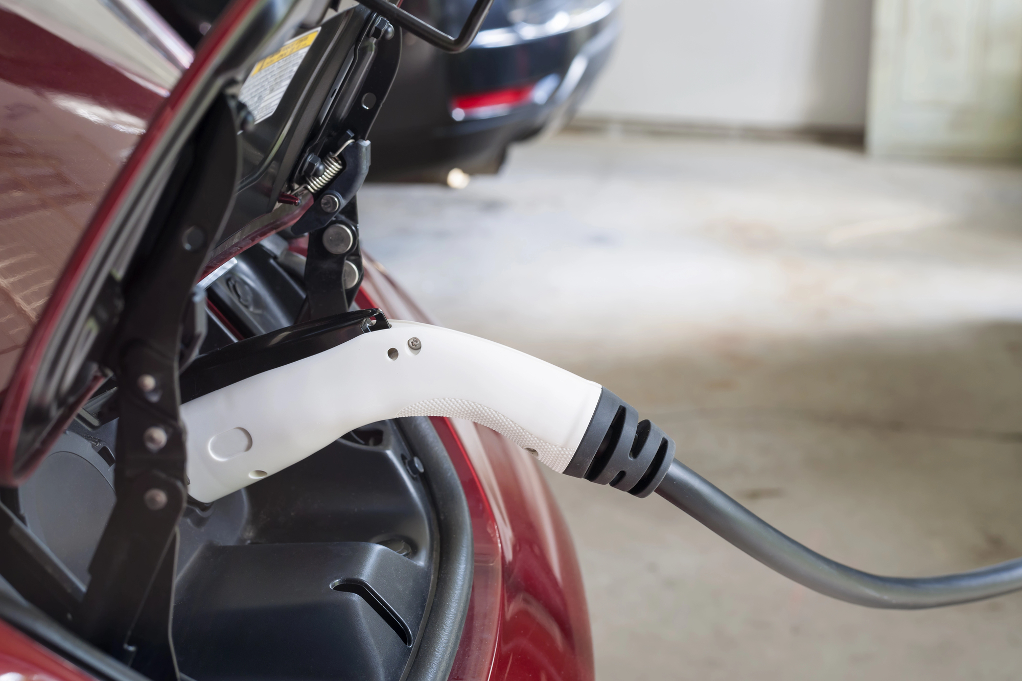 An electric vehicle is being charged in a garage, with a charging cable plugged into the car.