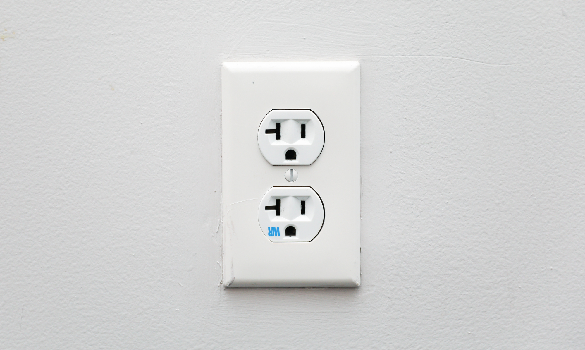 A white electrical outlet with two sockets is mounted on a plain white wall.