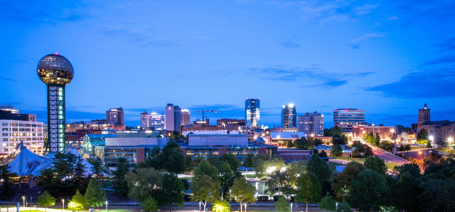 Knoxville, Tennessee skyline at dusk featuring illuminated downtown buildings and the Sunsphere above the city lights.