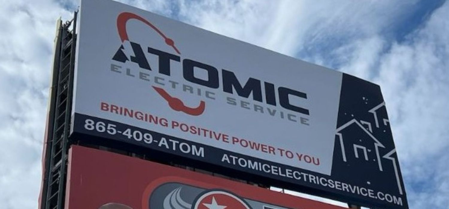 A billboard advertises Atomic Electric Service with the slogan "Bringing Positive Power to You" and contact details against a partly cloudy sky.